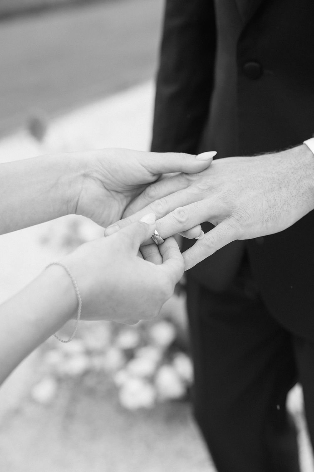 Close-up black and white shot of hands exchanging wedding rings during ceremony.