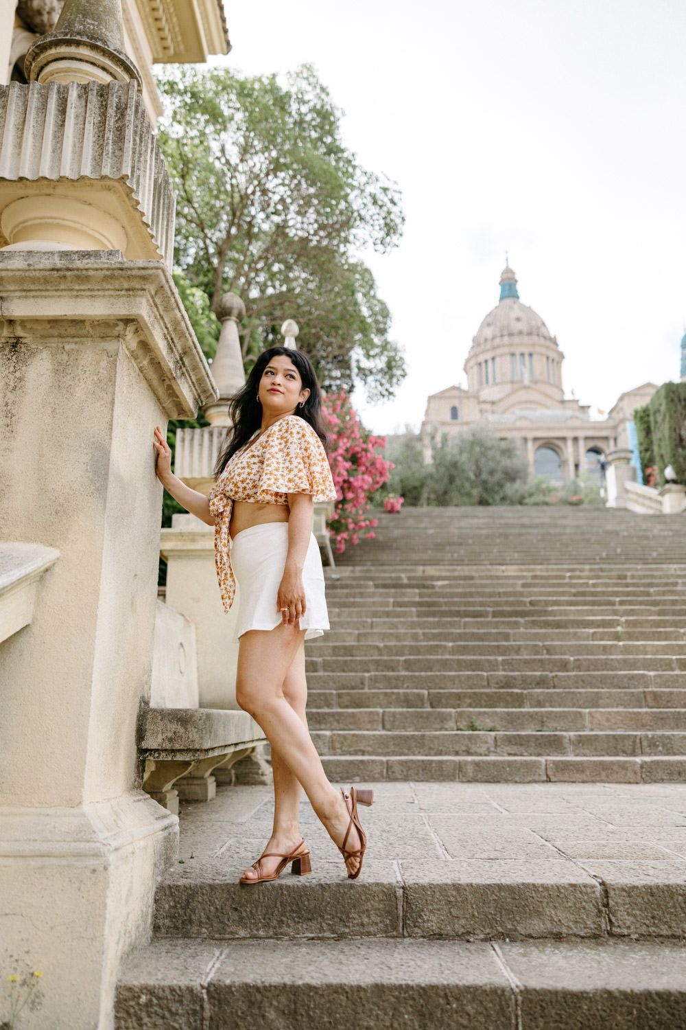 A person in summer attire poses on historic stone steps leading to a domed building.