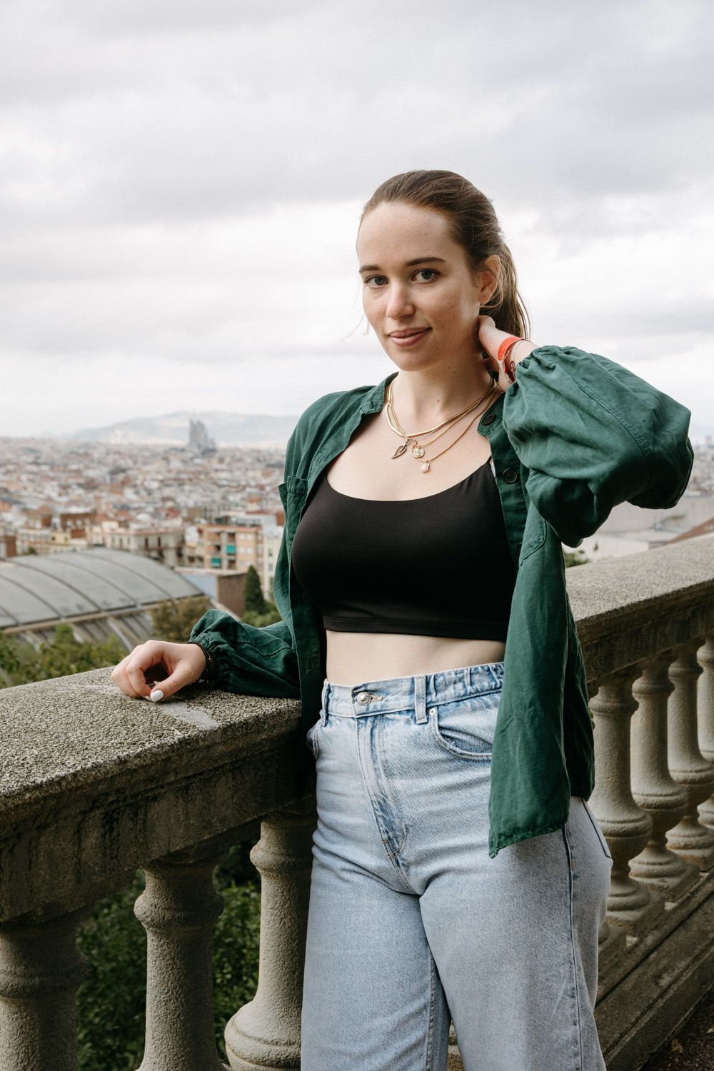 A person in casual attire poses against a stone balustrade overlooking a cityscape.