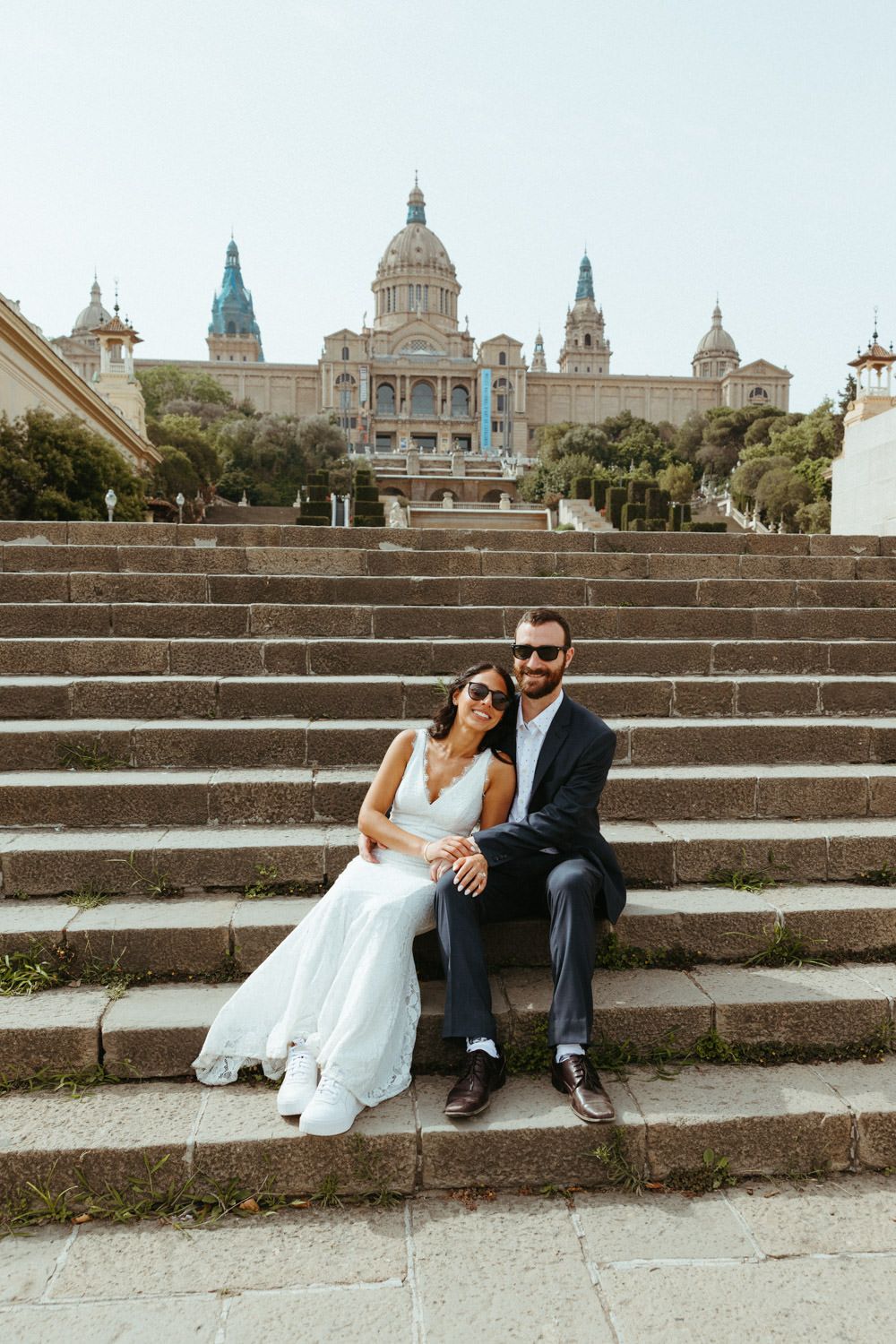 A couple in wedding attire sits on the steps of the National Palace in Barcelona.