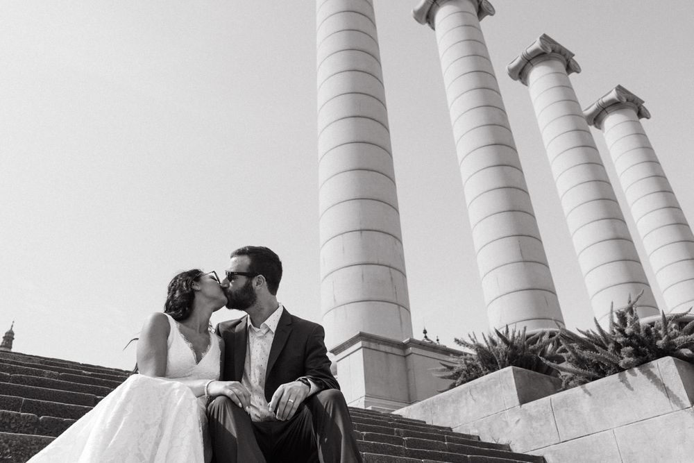 A romantic black and white photo of a couple sitting by architectural columns.