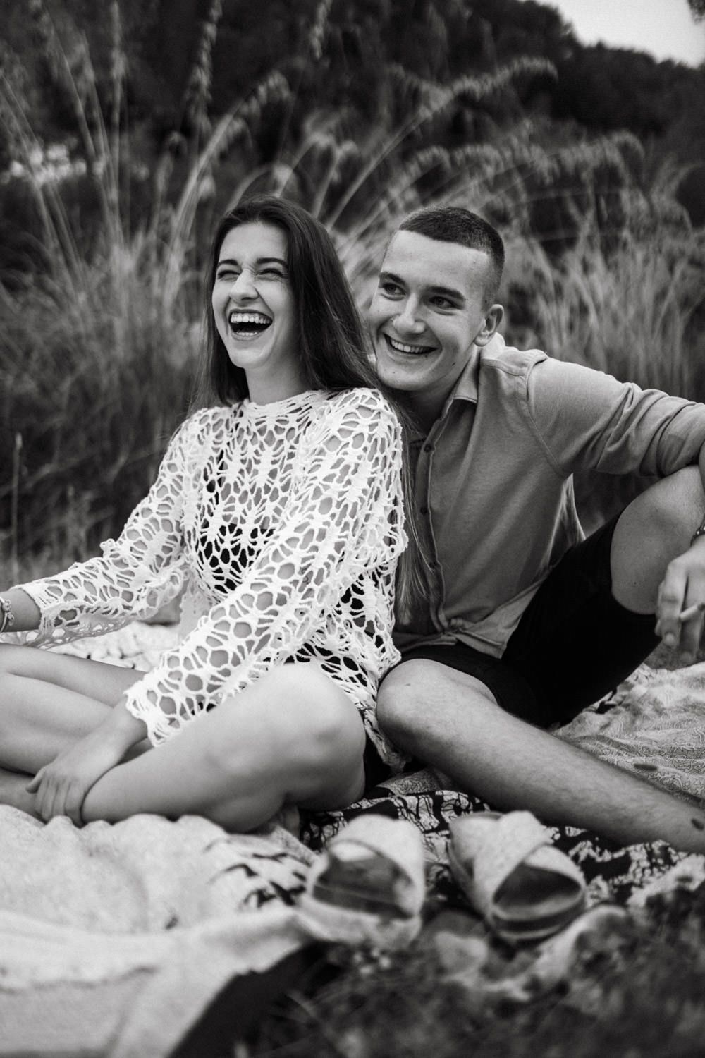 Couple shares joyful moments while lying on blanket outdoors in black and white.
