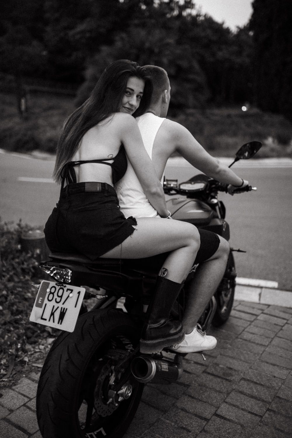 Stylish couple poses with motorcycle in dramatic black and white composition.