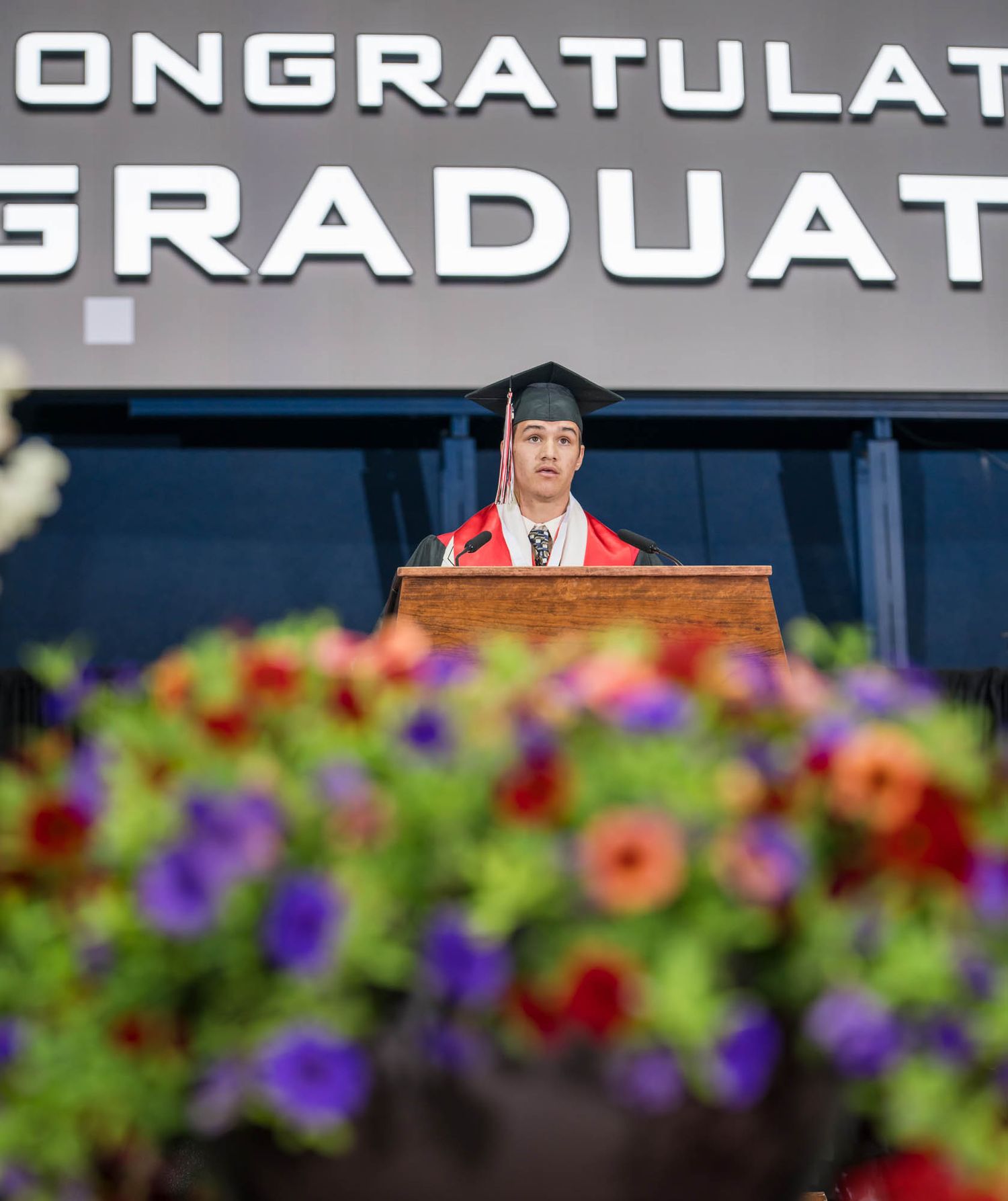 Logan Weidinger, standing at a podium, welcomed the 2025 CHS Graduation crowd in English.