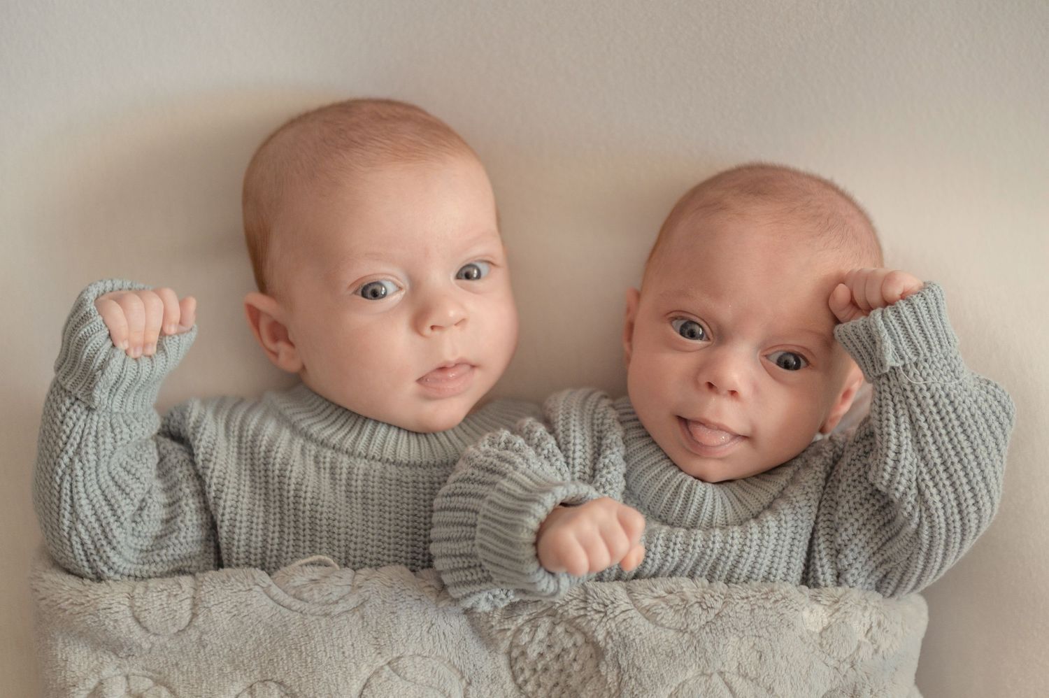 Two newborn twins in matching gray knit sweaters lying together on a soft blanket.