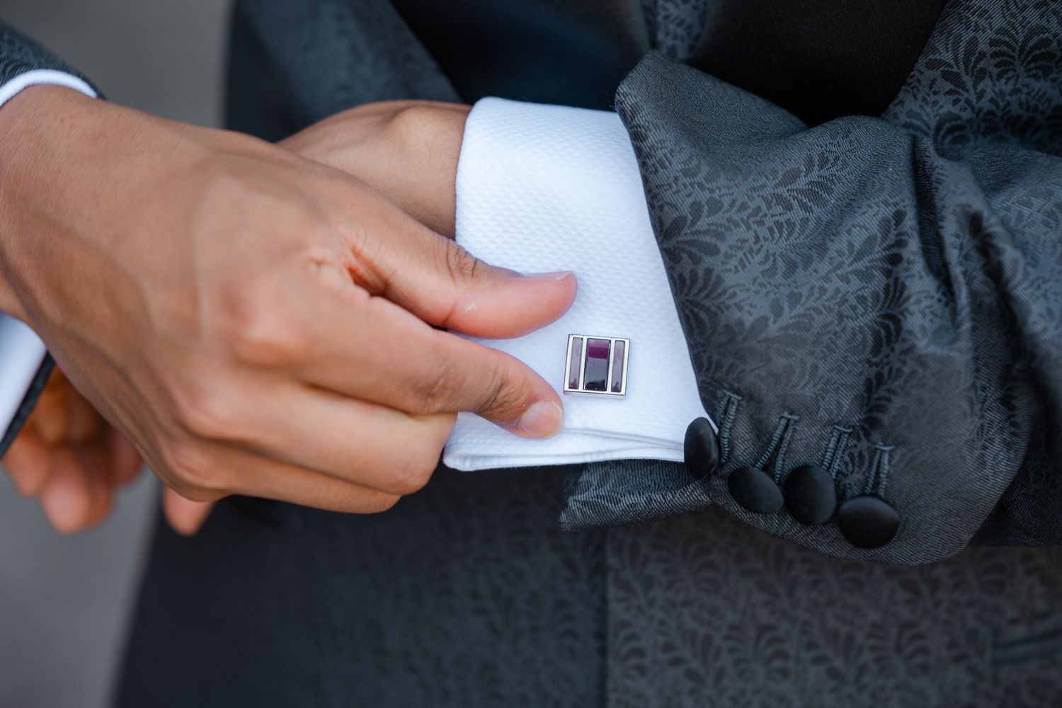 Close-up shot of hands adjusting silver cufflinks on a formal black suit sleeve.