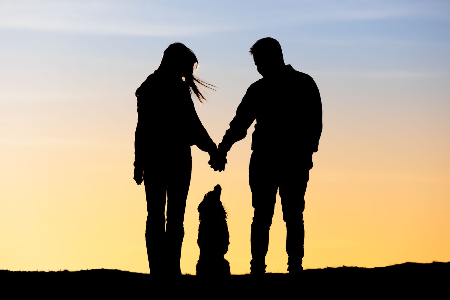 Silhouettes of people walking together against a vibrant sunset sky on a hilltop.