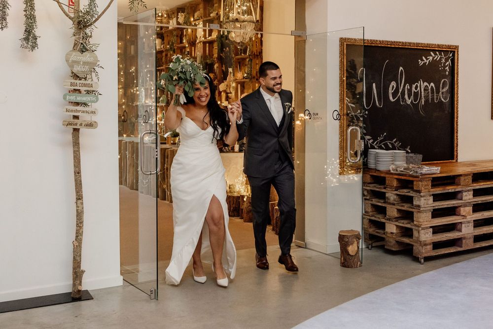 A couple in formal wedding attire walks through a modern industrial venue with exposed brick walls and wooden pallets.