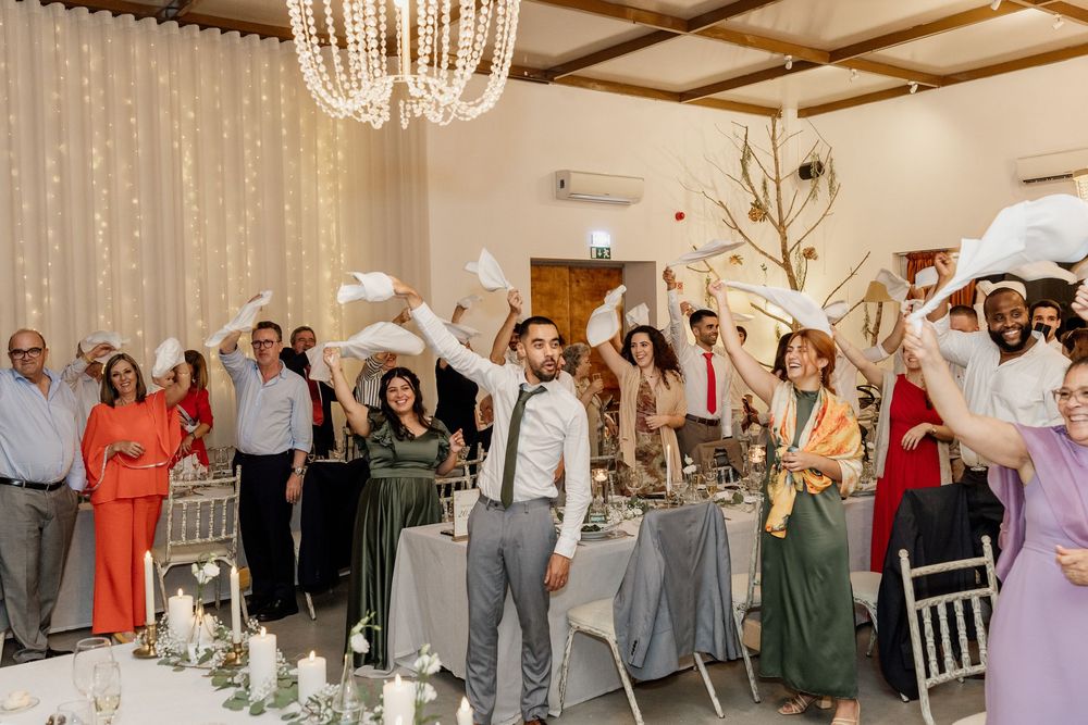 Wedding guests mingle and socialize during an elegant reception in a light-filled room with crystal chandeliers.