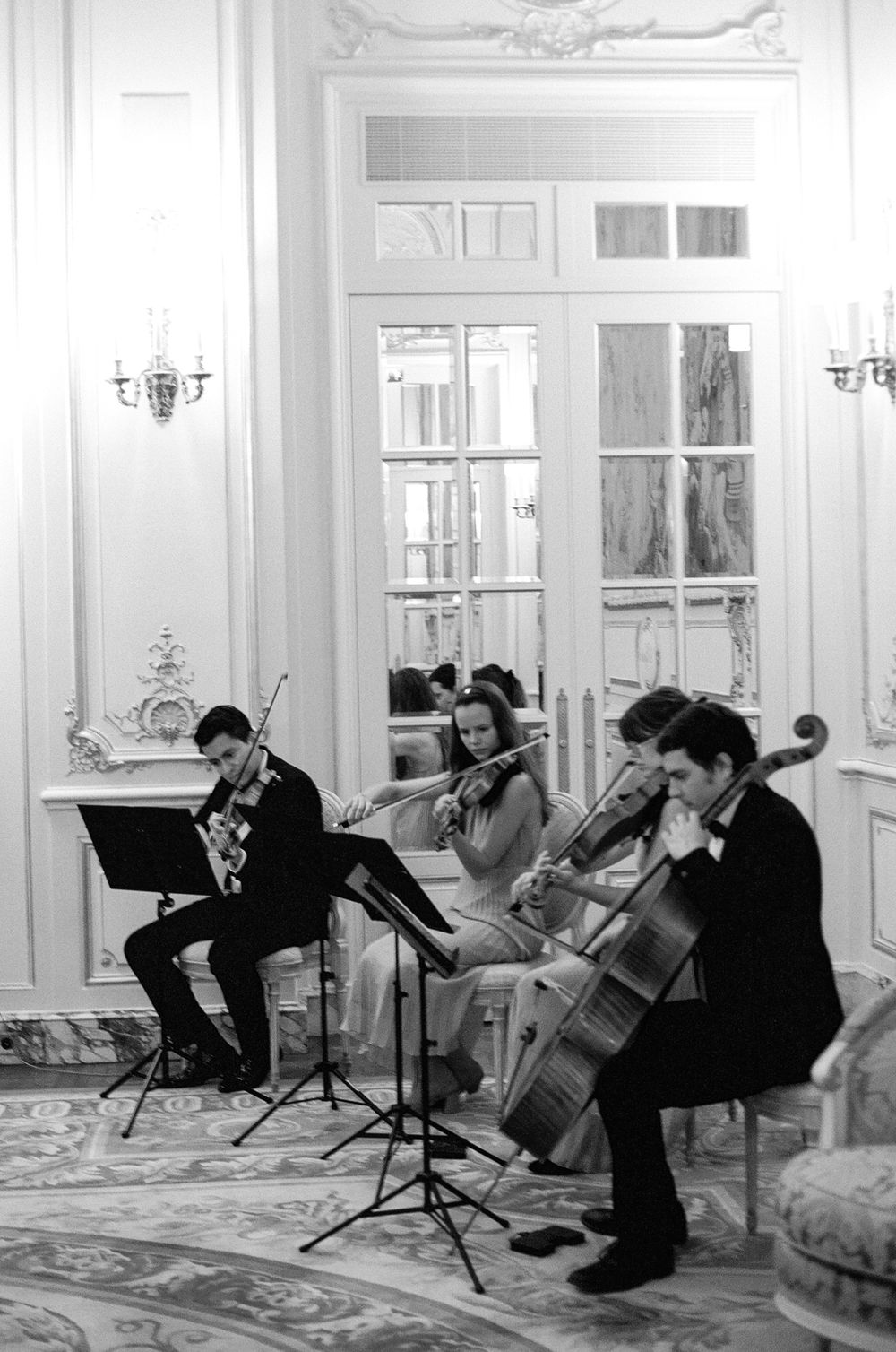 String quartet performing in grand white ballroom with ornate moldings, musicians playing violin and cello in black and white.