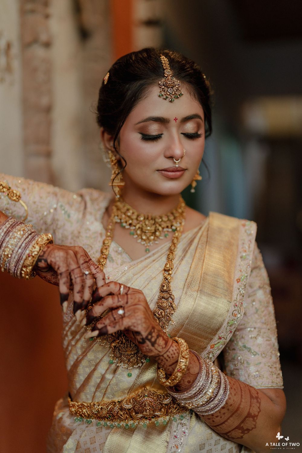 Close-up of bridal hands adorned with mehndi and gold jewelry against cream colored fabric.