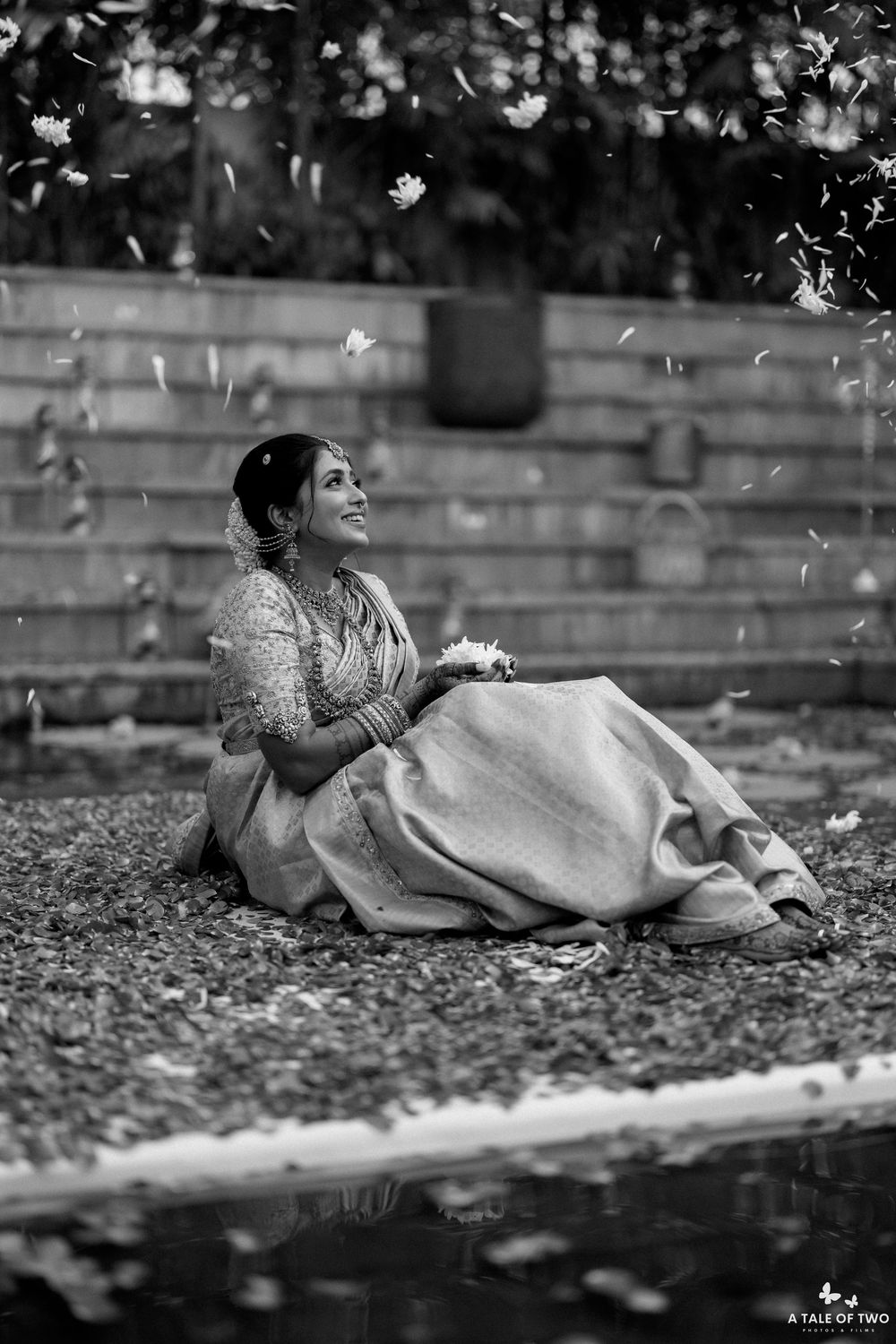Black and white portrait of person lying on ground with flower petals falling in artistic composition.