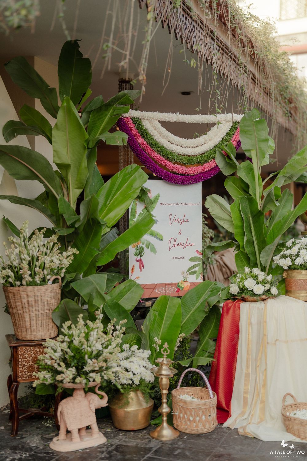 Tropical wedding decor setup with banana leaves, white flowers and colorful garlands.