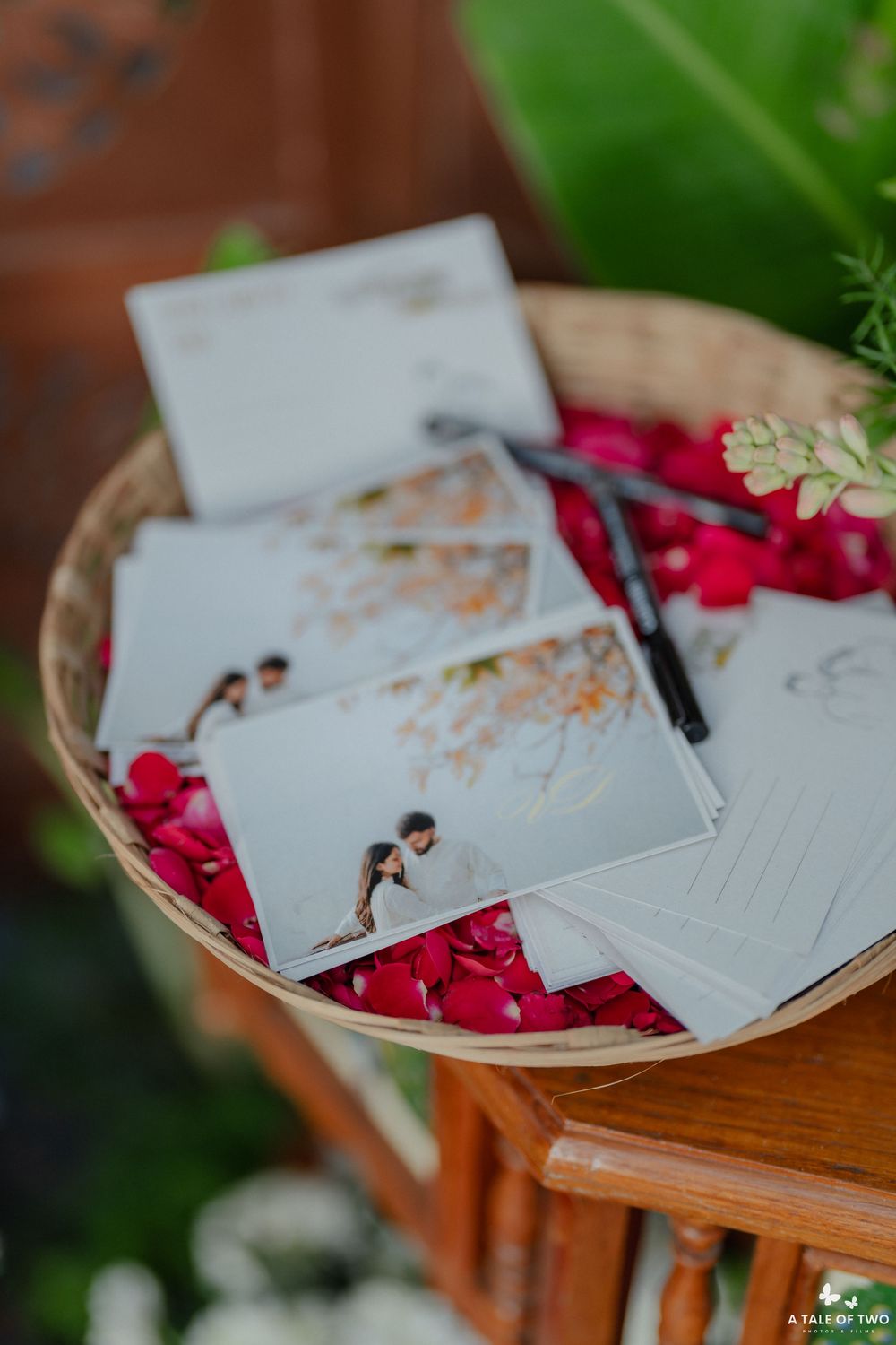 A wooden table holds scattered papers and red rose petals with a pen for writing.