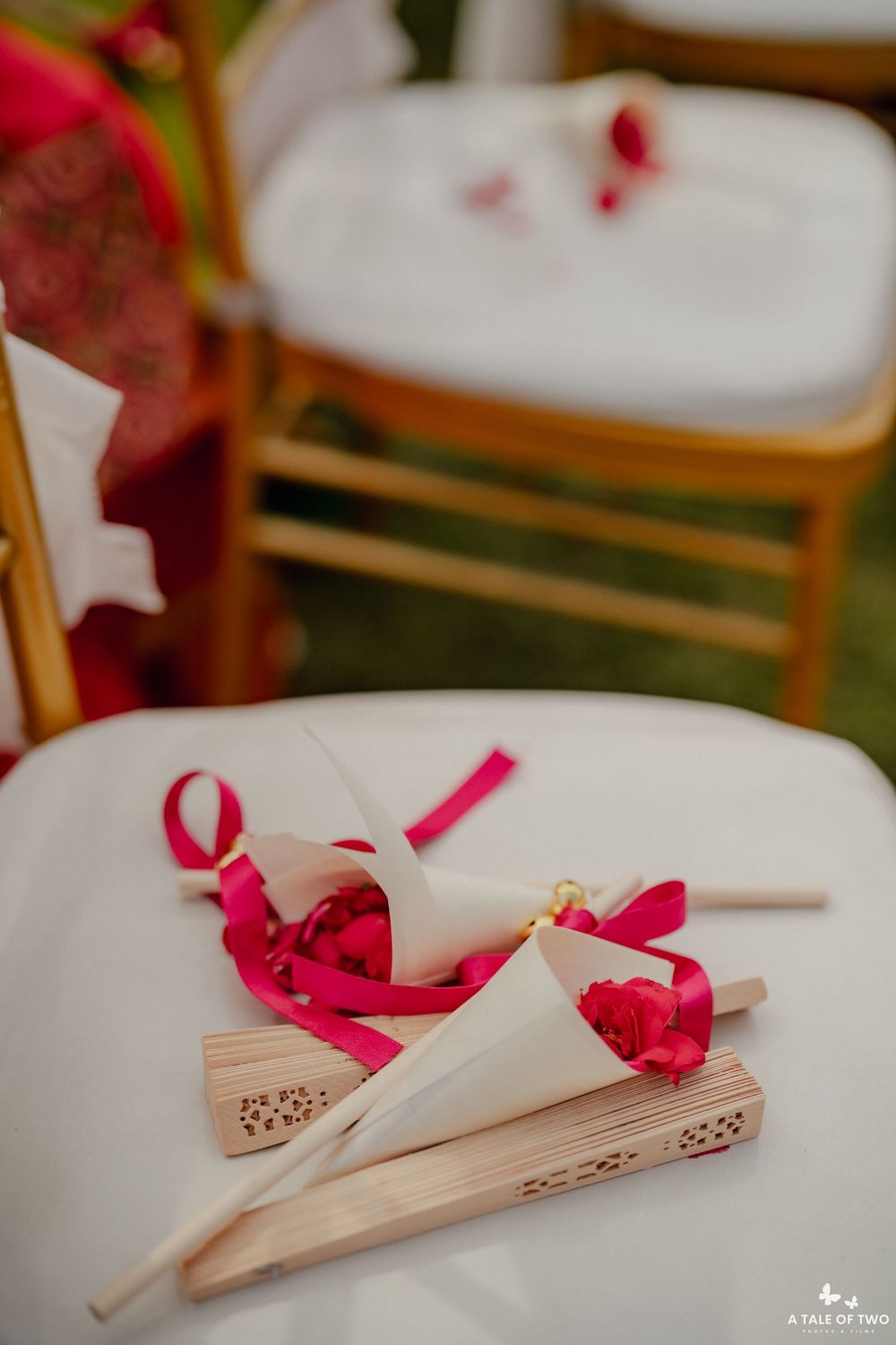 Decorative wedding programs or menus tied with red ribbons arranged on white chairs.