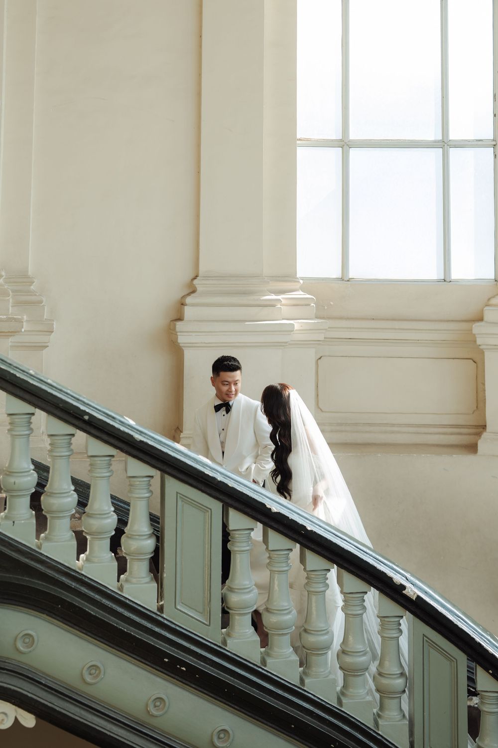 Bride and groom share romantic moment on grand staircase in bright elegant venue.