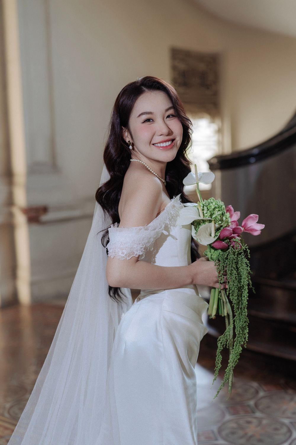 Radiant bride in off-shoulder gown holds cascading pink and white bouquet on staircase.