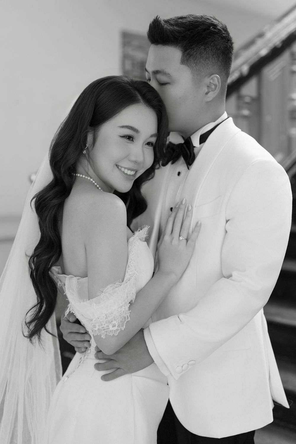 Black and white photo of groom kissing brides cheek as she smiles in his embrace.