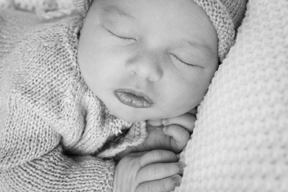 A series of black and white close-up photos showing a sleeping newborn baby in soft blankets.