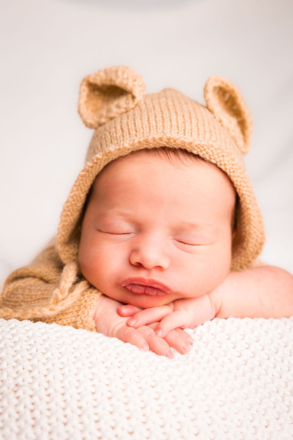 Sleeping newborn wearing knit bear hat in sequence of three peaceful close-up portraits on white blanket.