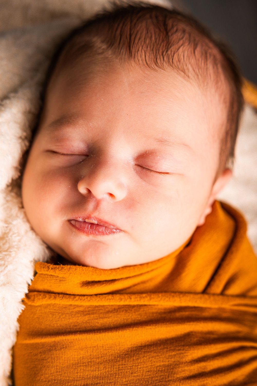 Close-up photo series of a sleeping newborn baby wrapped in a warm orange blanket.