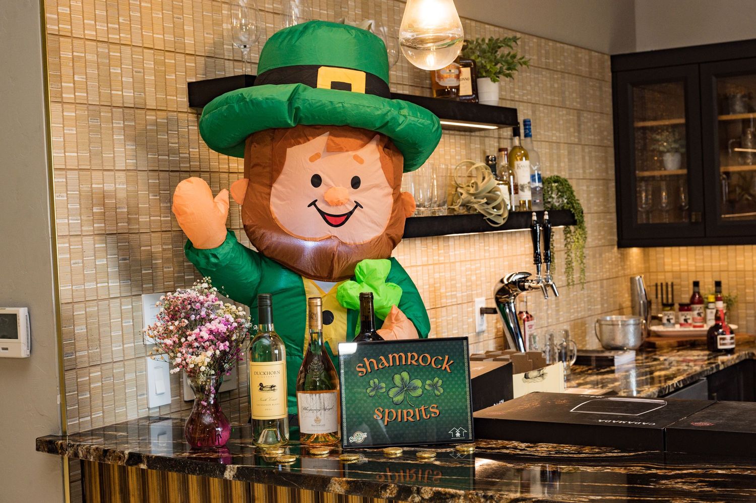 Inflatable leprechaun decoration at a bar counter with a Shamrock Spirits sign and wine bottles.