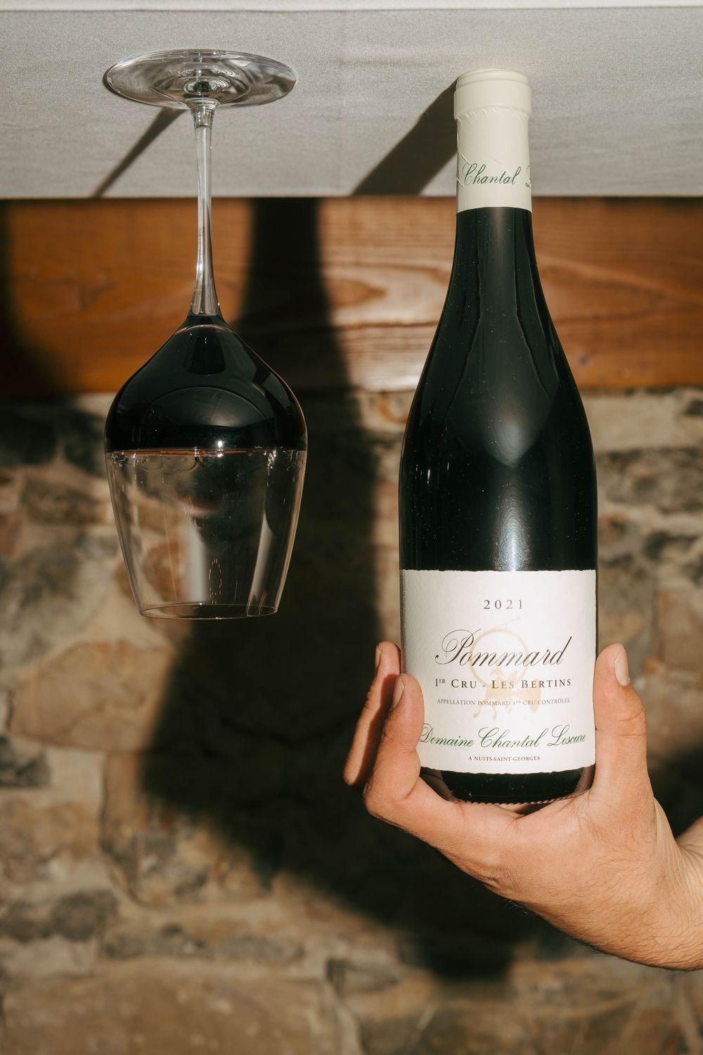 Main tenant une bouteille de vin rouge Pommard 1er Cru Domaine Chantel Lescure 2021 avec un verre à vin inversé au-dessus.
