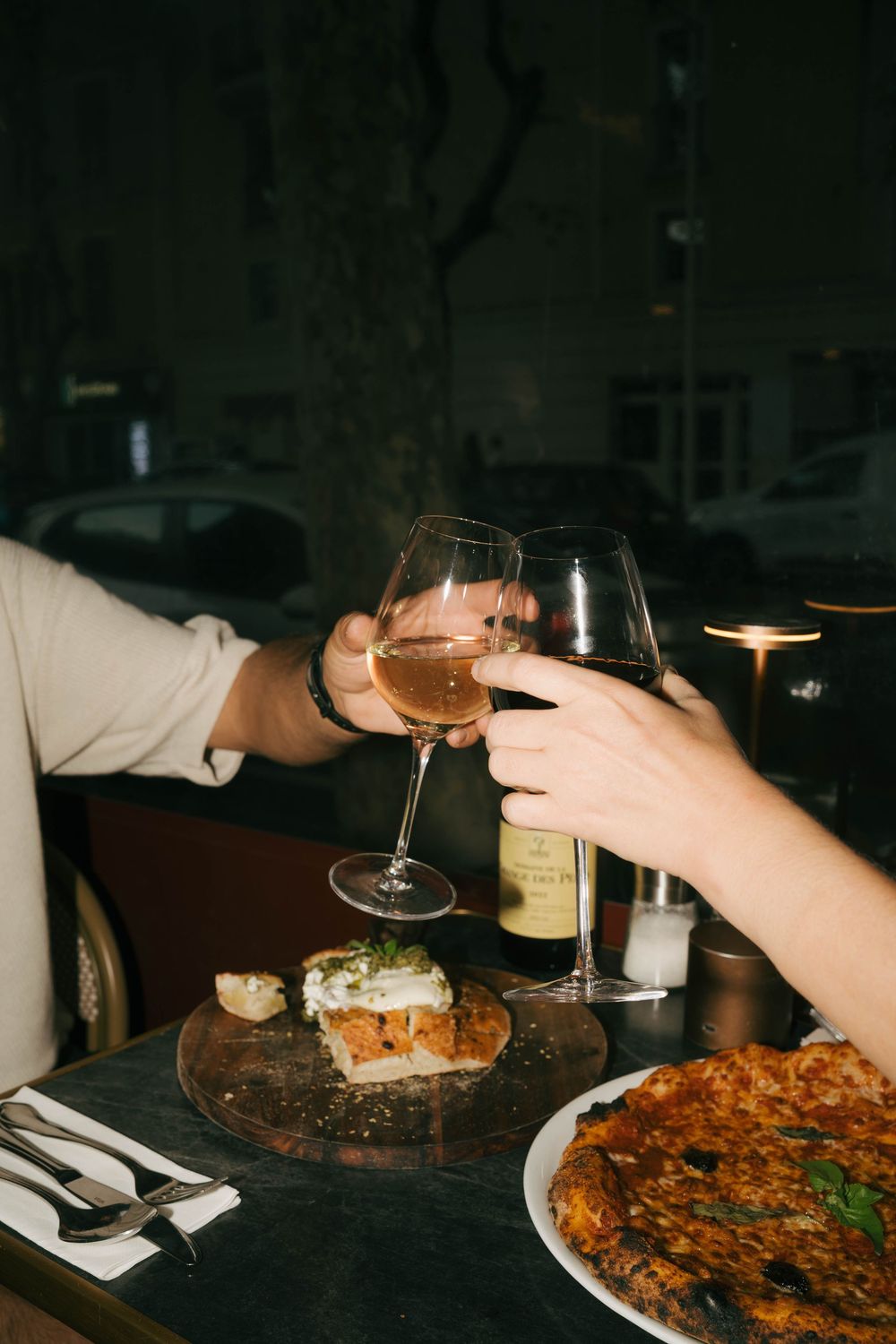 Deux personnes faisant claquer des verres à vin sur une table de restaurant aux chandelles avec des plats lors d'un dîner romantique.