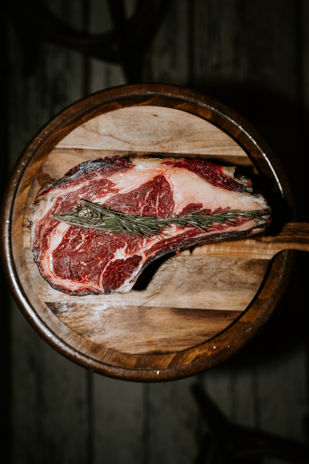 Steak de faux-filet cru au romarin sur une planche à découper en bois rustique, assaisonné de sel.