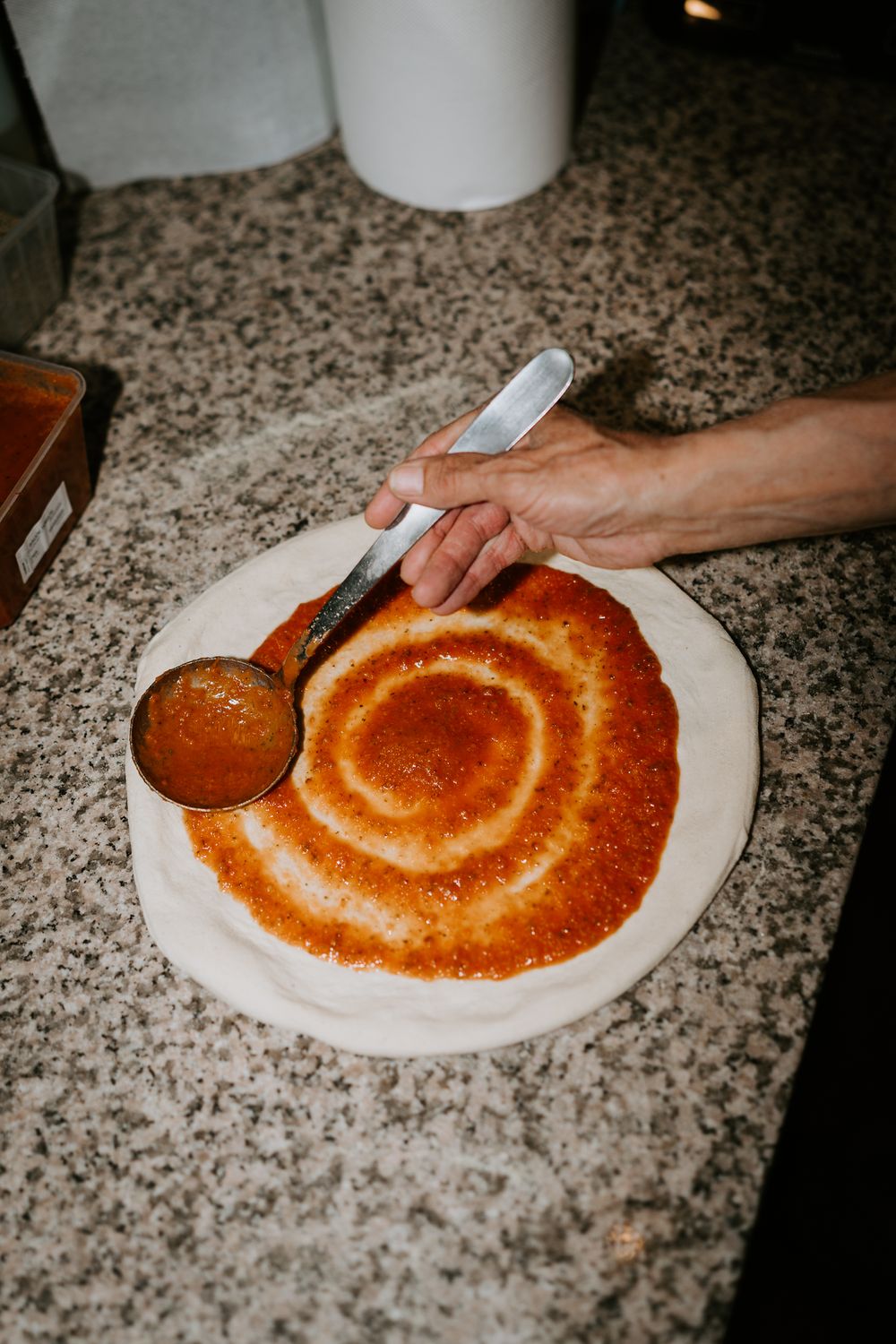 Le chef étale la sauce tomate en mouvement circulaire sur la pâte à pizza fraîche sur une surface de marbre.