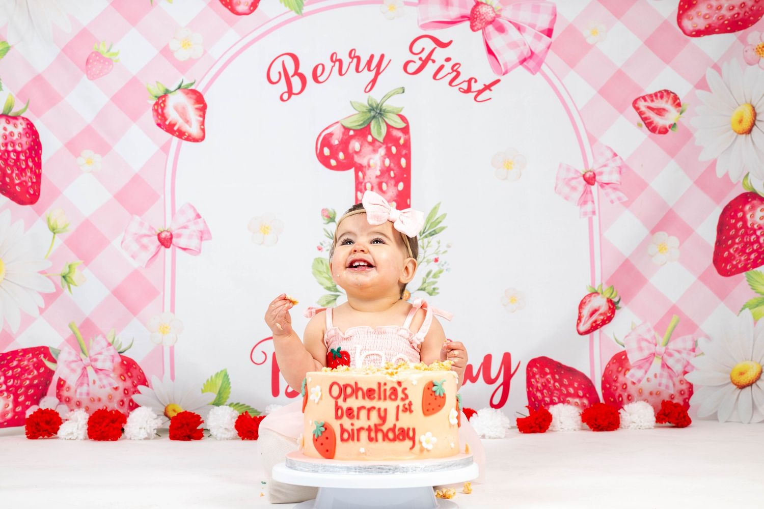 Pink and white strawberry themed first birthday party setup with cake and festive decorations.