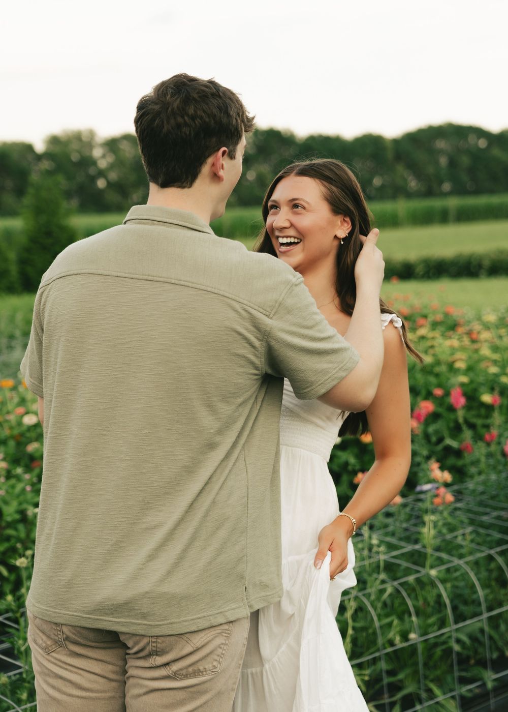 Couple laughing and dancing together in a flower garden during an outdoor engagement photo session.