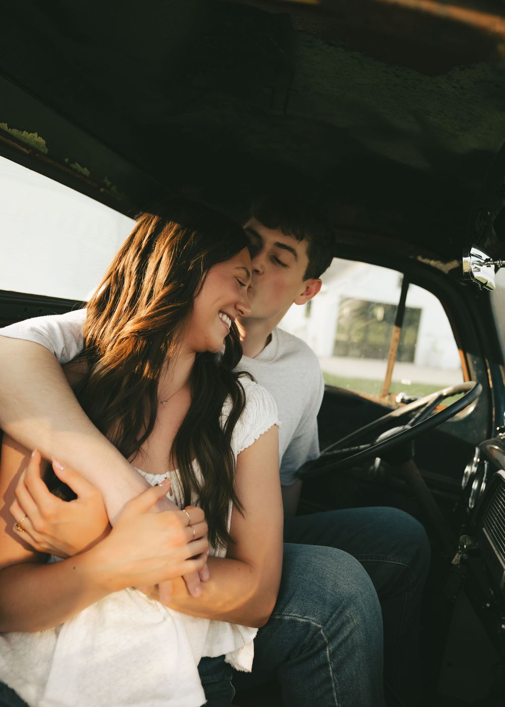 A couple sharing a romantic moment inside a vintage car, embracing and smiling close together.