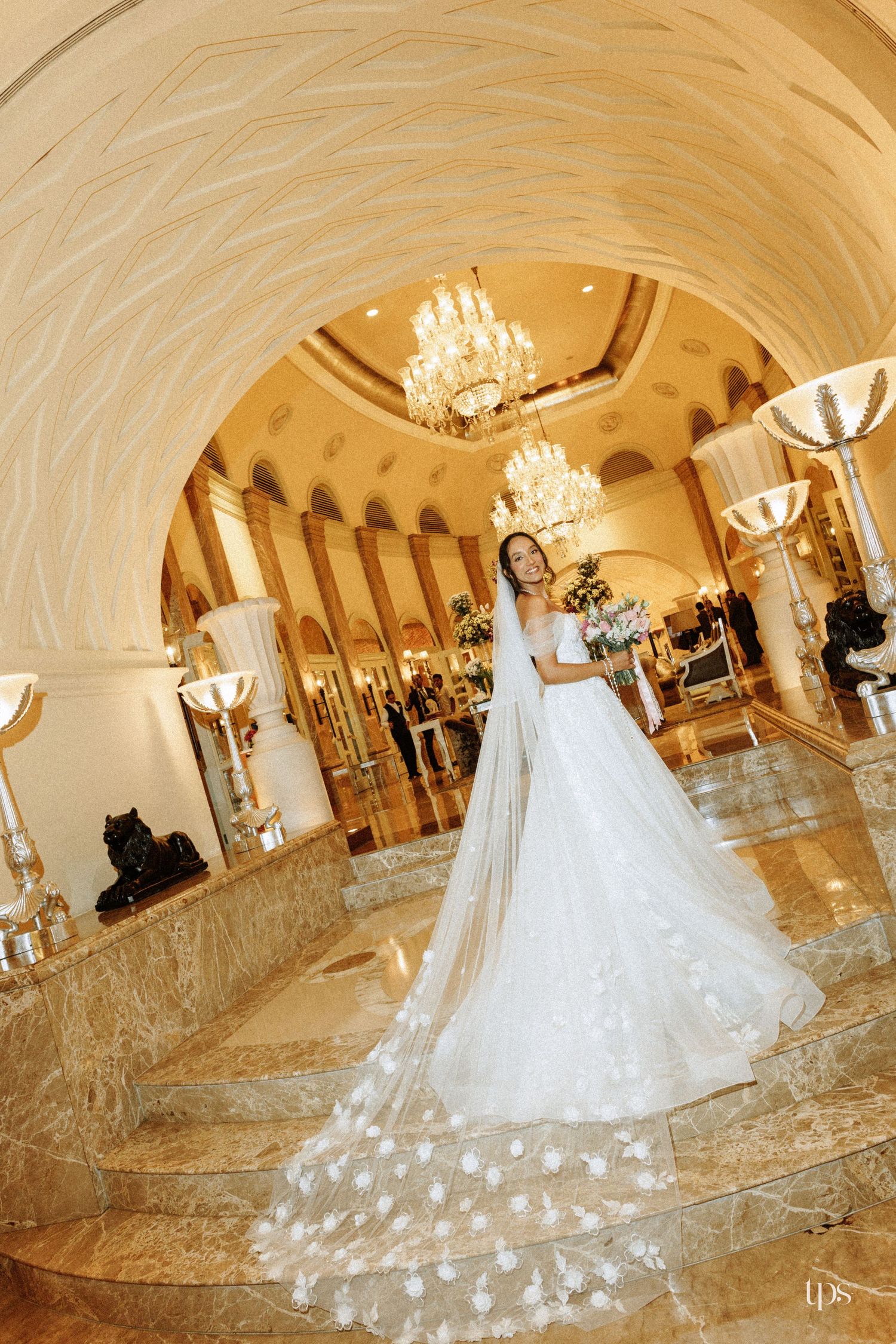 Bride in white gown with floral veil on marble steps under a chandelier elegantly captured by a wedding photographer in Sydney, Gold Coast
