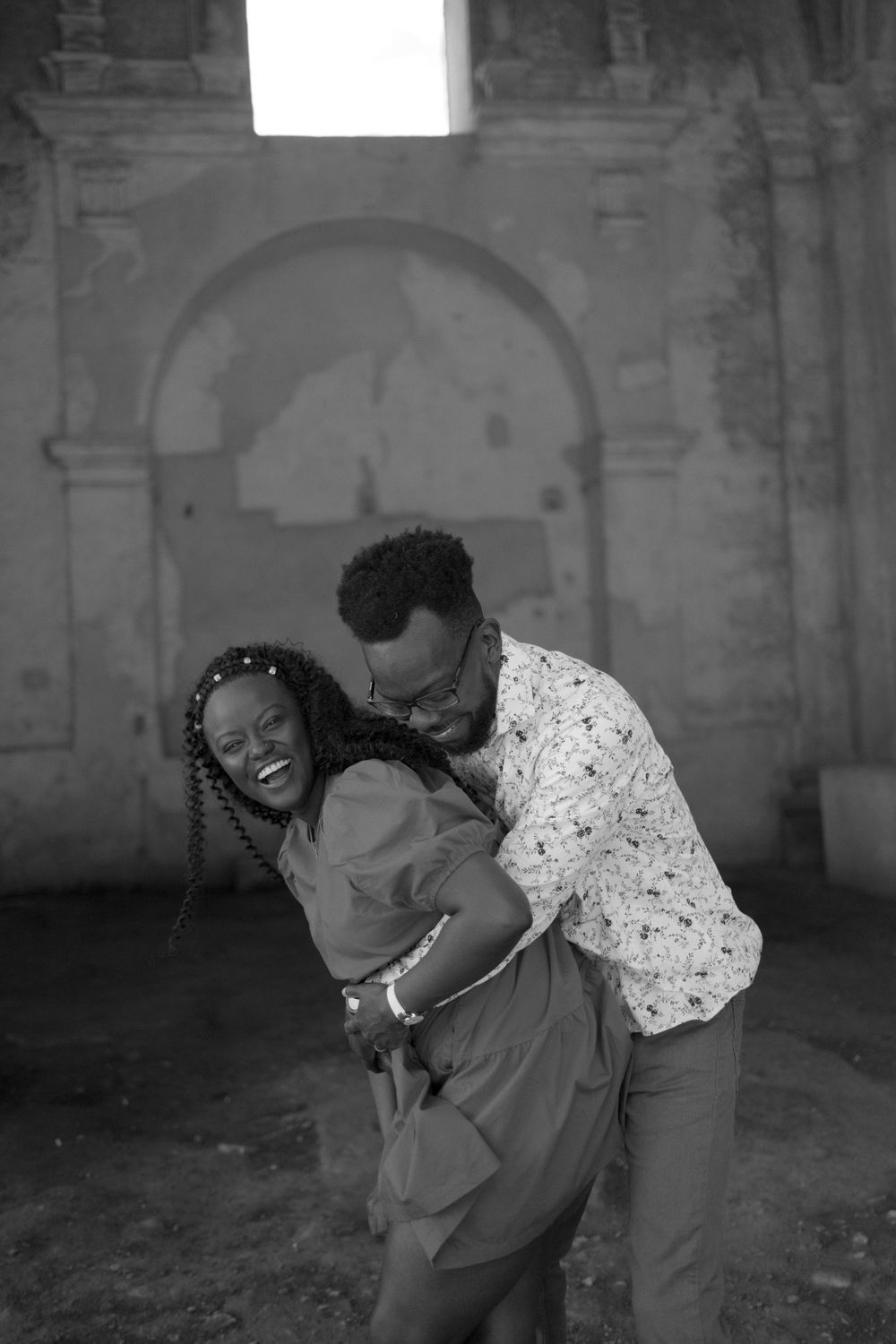 Joyful couple embracing and laughing inside historic ruins in black and white photo.