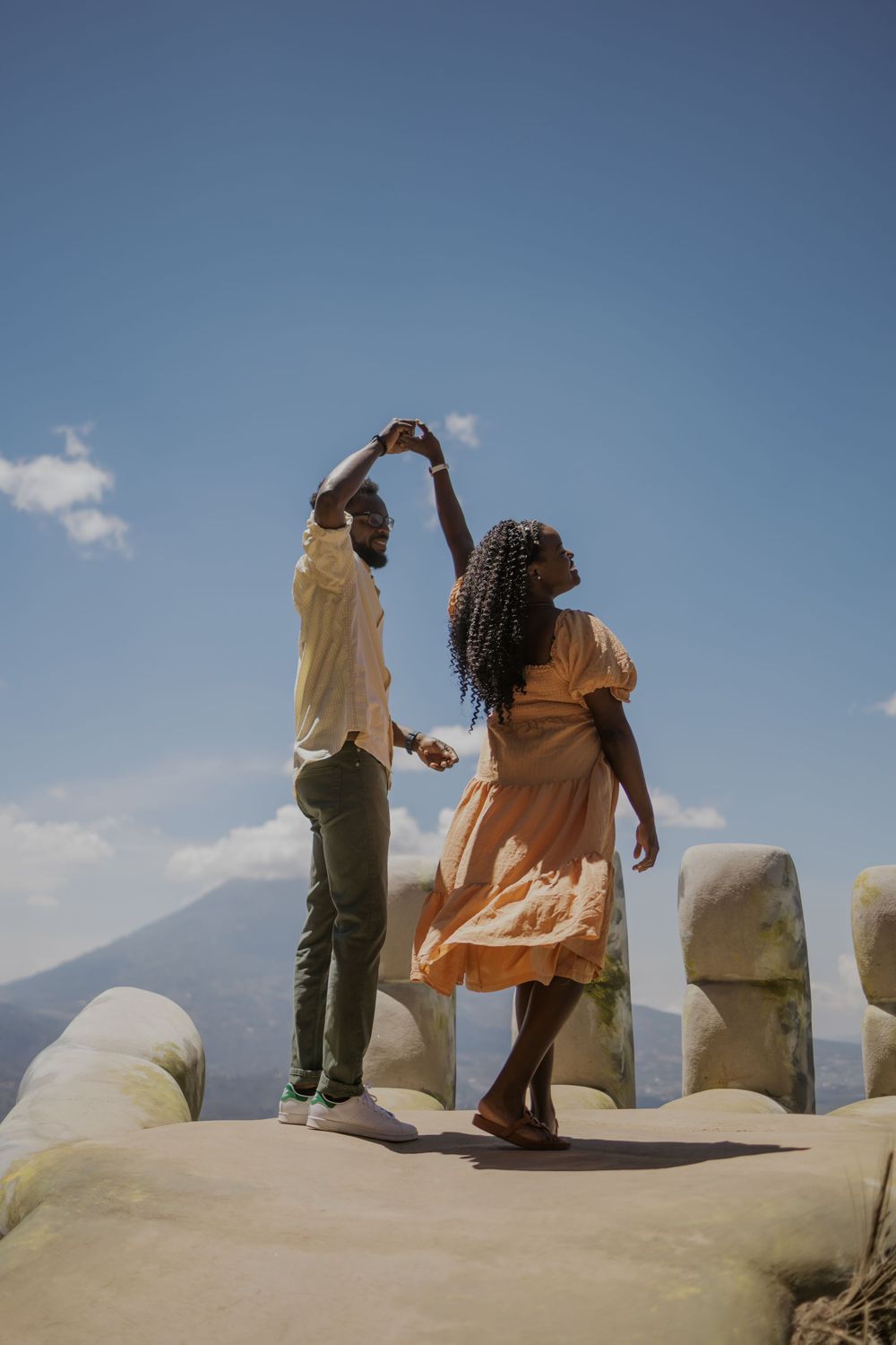 Joyful couple dancing outdoors on a scenic overlook with mountains and blue sky.