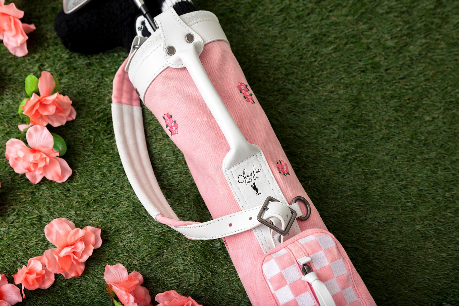 Pink and white golf clubs laid on artificial grass with scattered pink floral decorations.