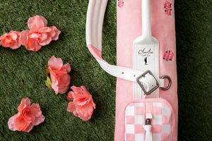 Pink golf bag with floral accents and matching coral flowers arranged on green grass creates an elegant composition.