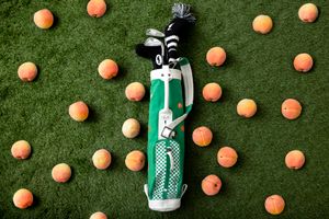 Golf club head surrounded by scattered orange golf balls on artificial green turf.