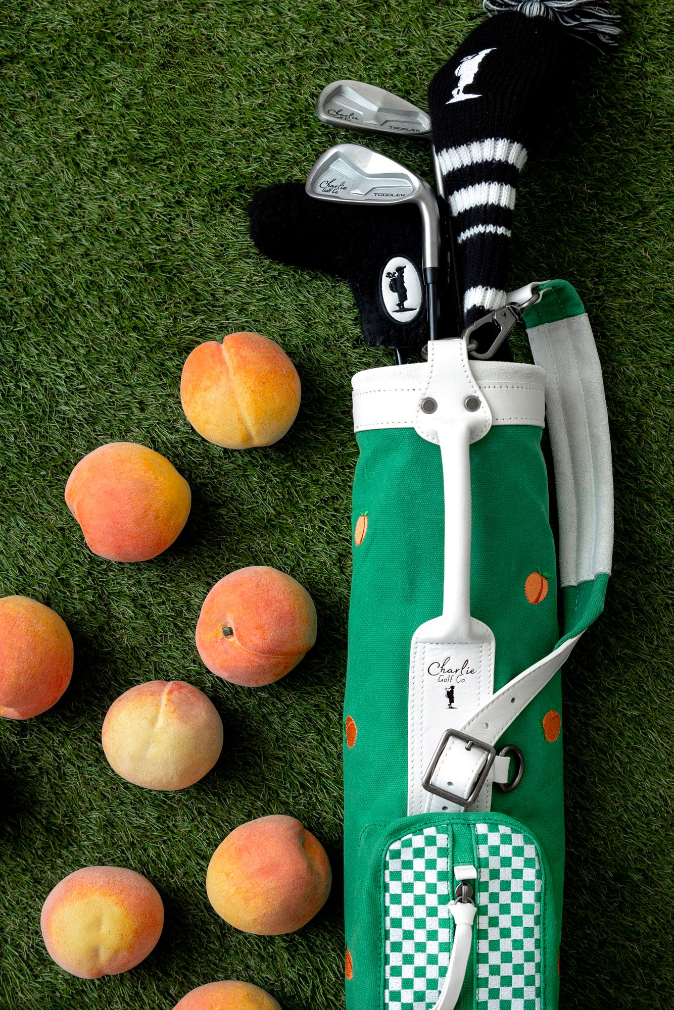 Fresh peaches arranged beside a green golf club bag with checkered pattern on grass.