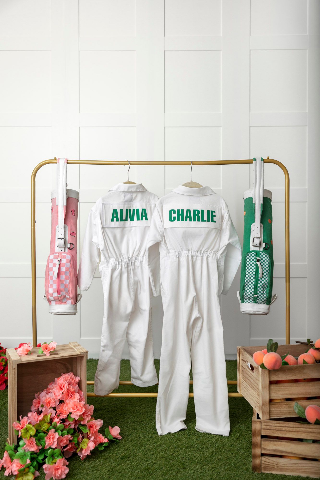 White jumpsuits hang on gold clothing racks with wooden crates and pink flowers creating a garden party display setup.