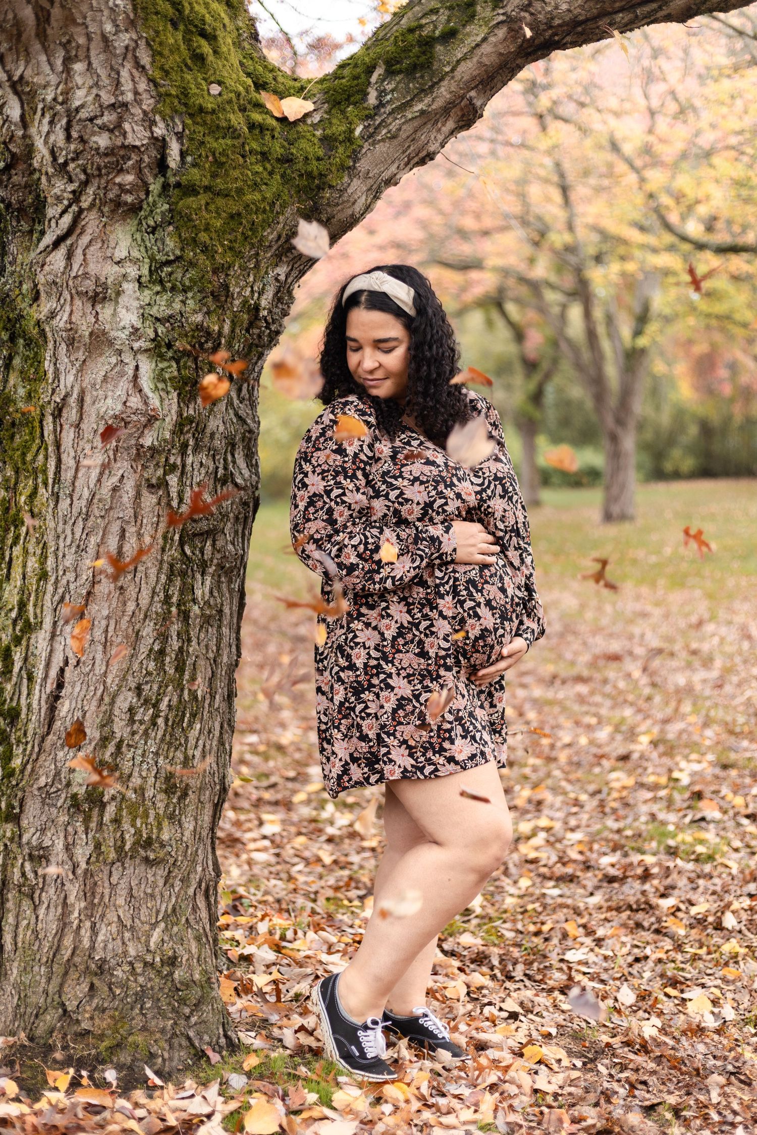 Person in floral top poses playfully among fallen autumn leaves and trees.