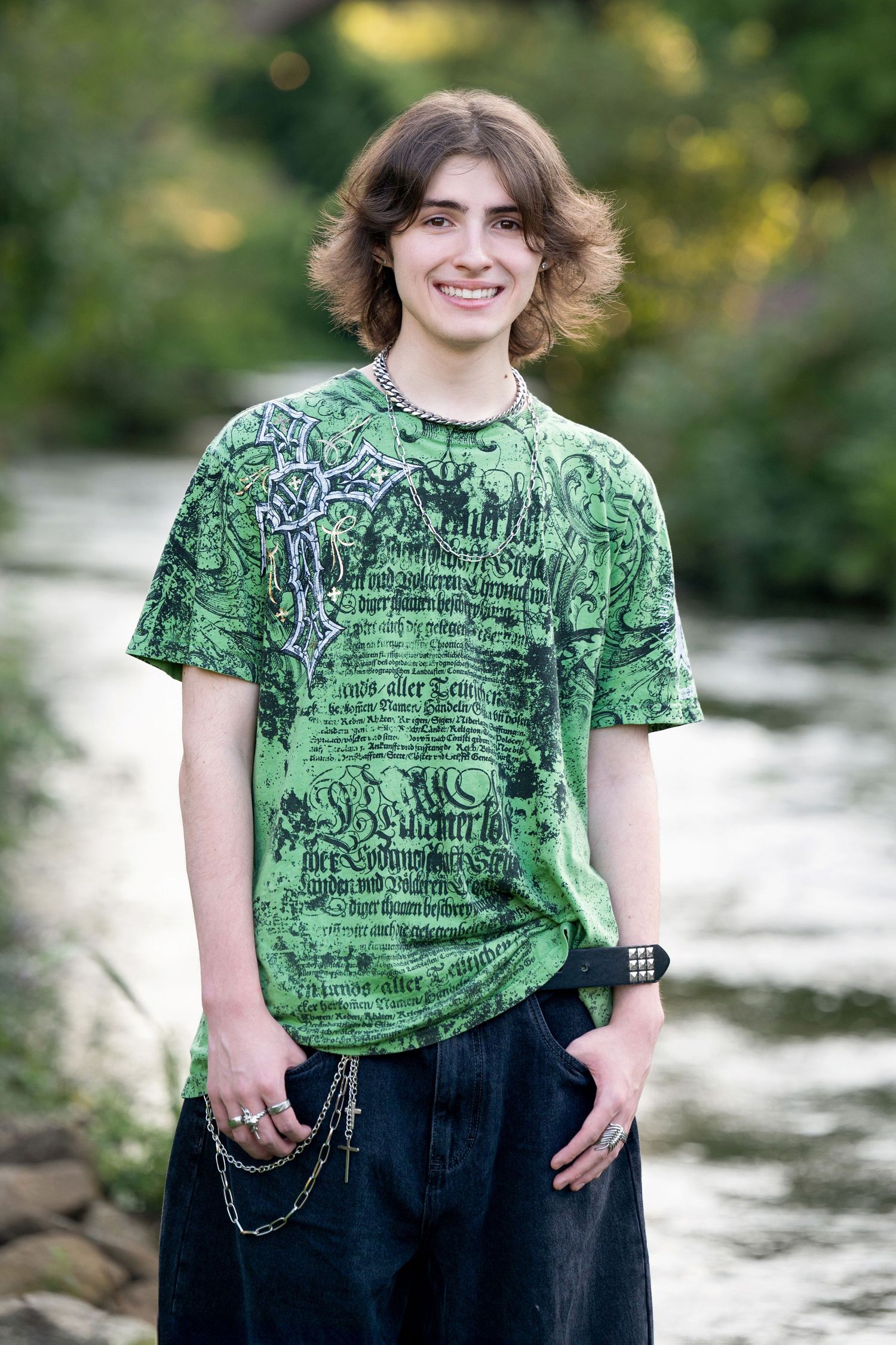 A person in a light blue button-down shirt and khaki shorts poses casually against a coastal backdrop with tall grass.