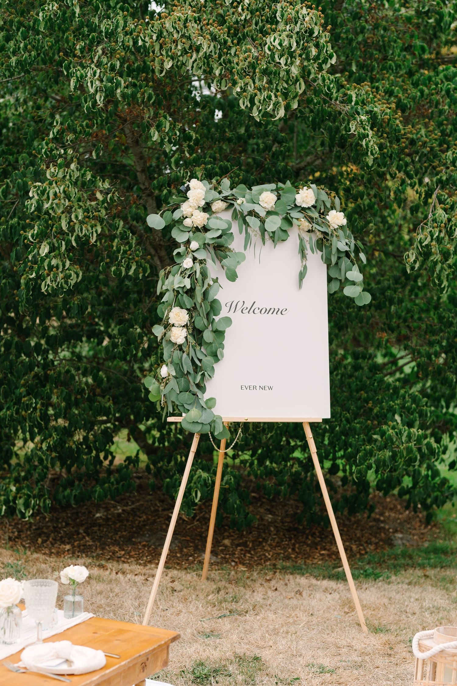Welcome sign display with greenery decorations set up on wooden easels against a lush garden backdrop.