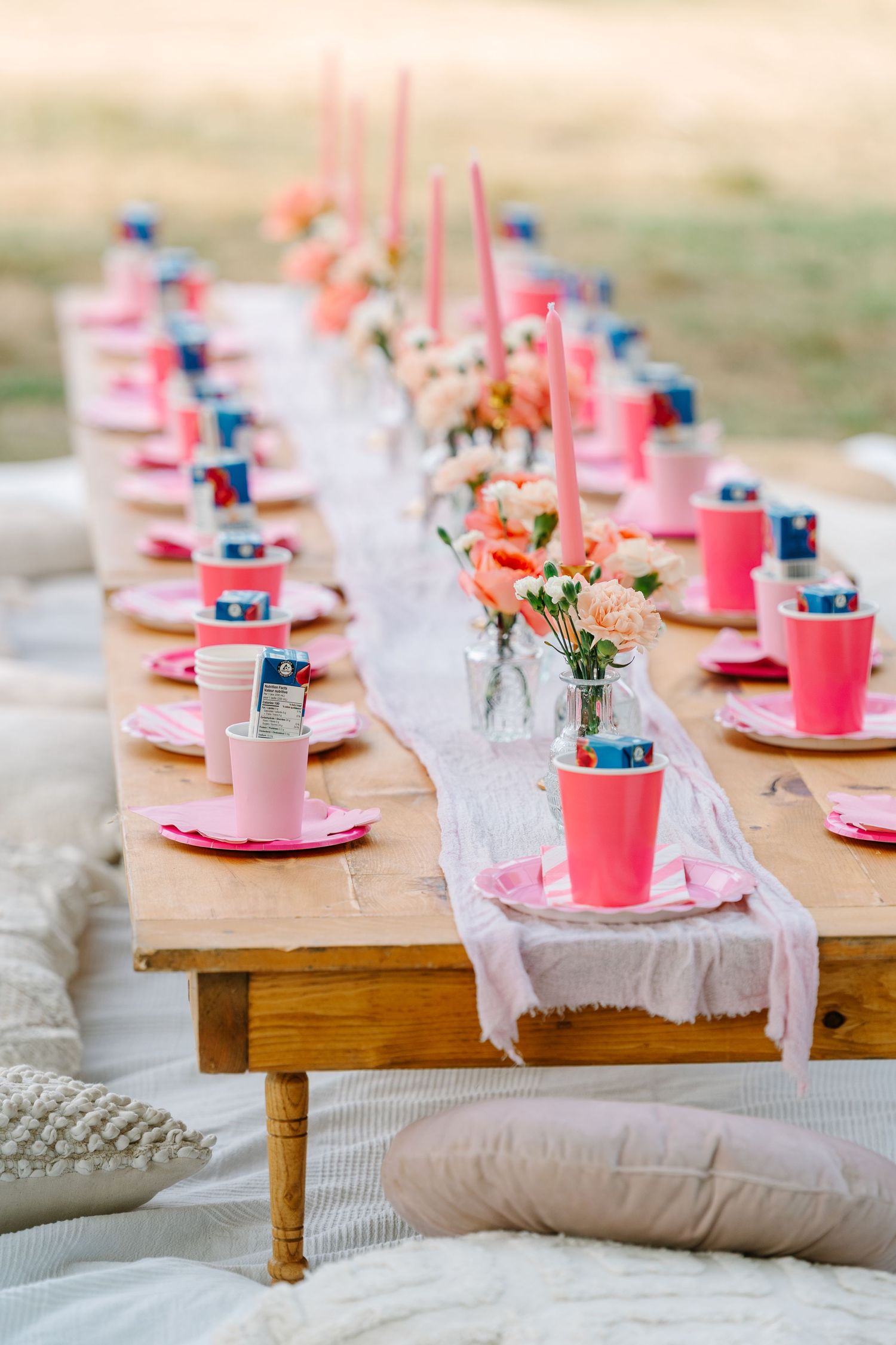 Rustic wooden table set with pink party decorations, white lace runner, and small floral centerpieces for a festive celebration.