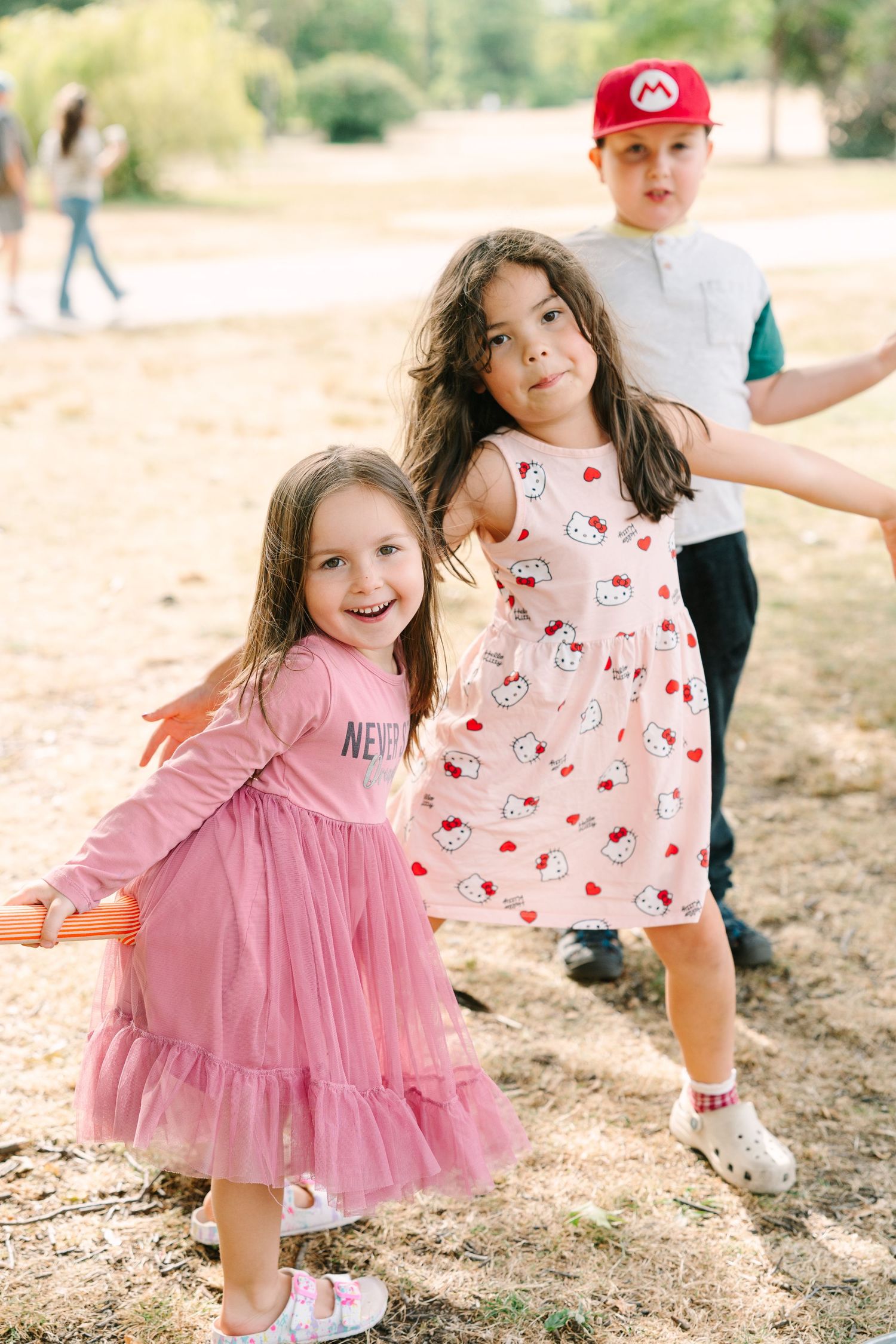 Children playing outdoors in pink dresses and casual wear during a sunny day.