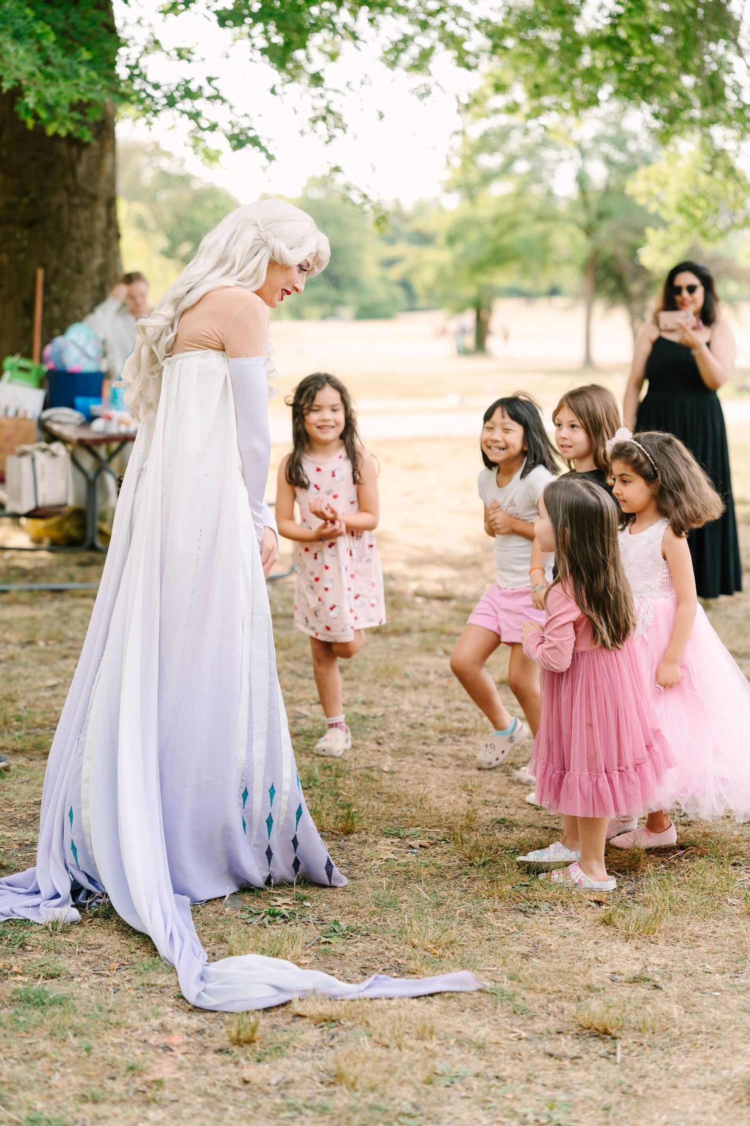 Children in pink and white dresses playing near a draped white cloth outdoors.