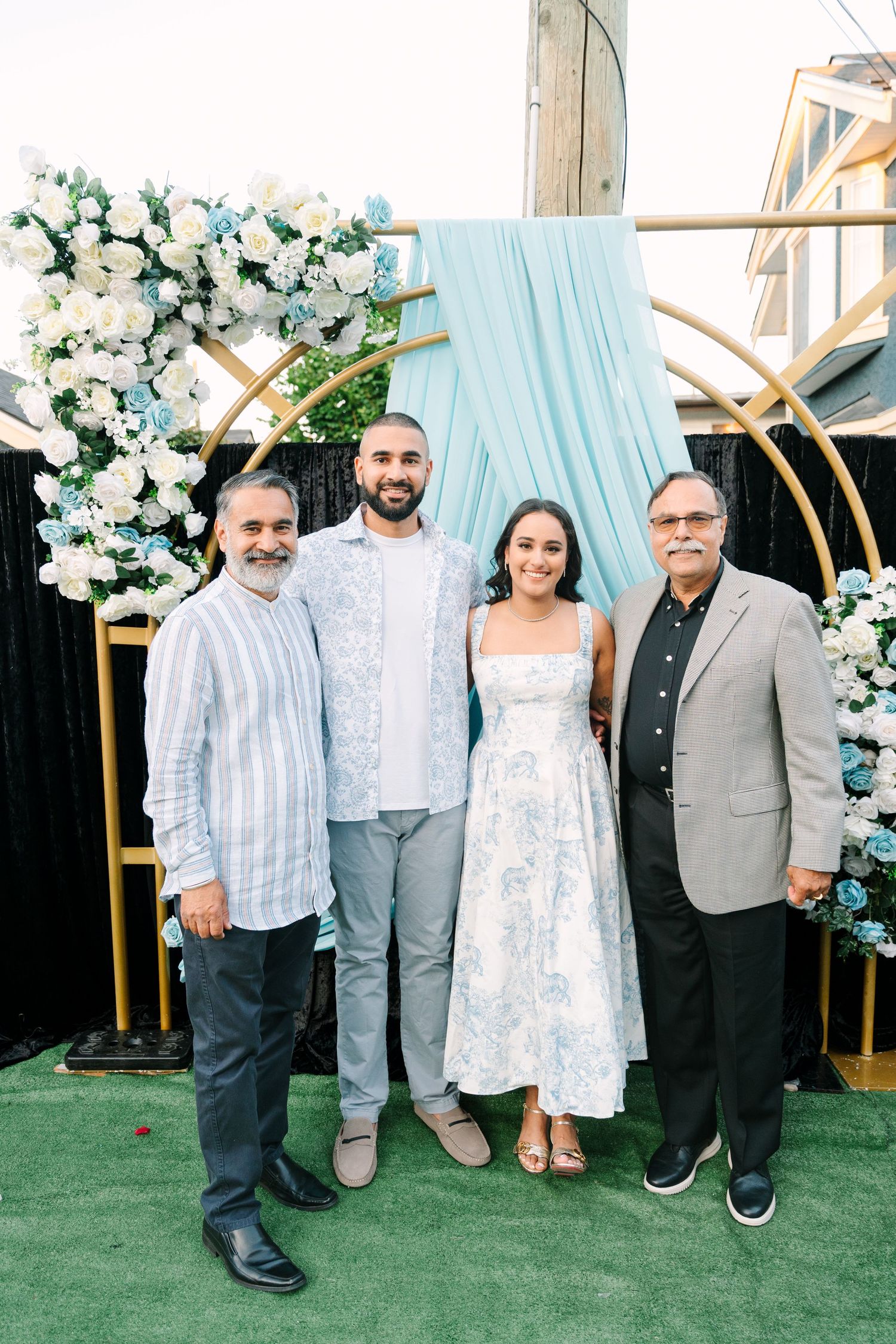 Group photo at outdoor event with floral arch backdrop and artificial grass floor.