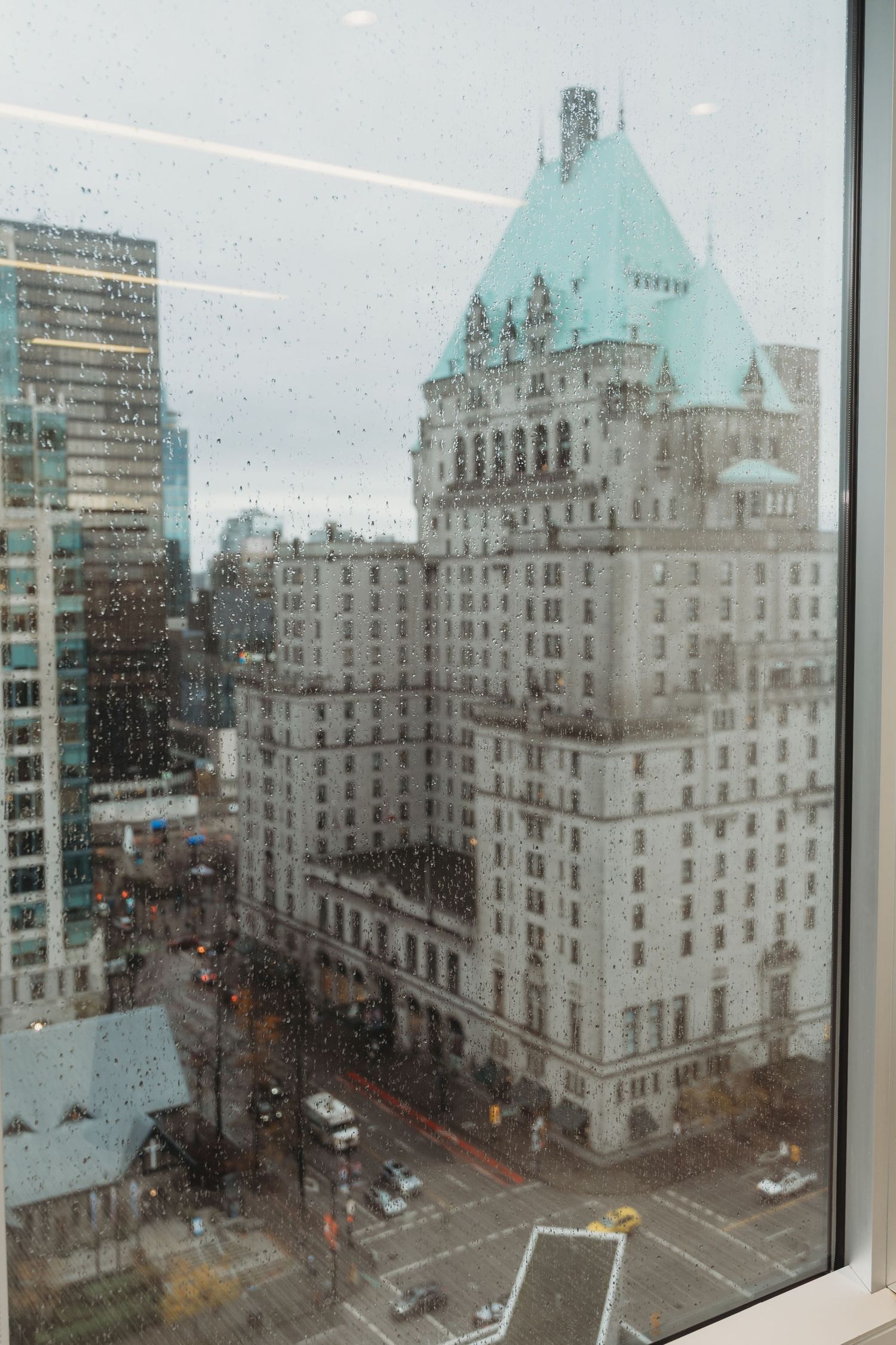 View through a rainy window of historic Hotel Vancouver with its iconic green copper roof and Gothic architecture.