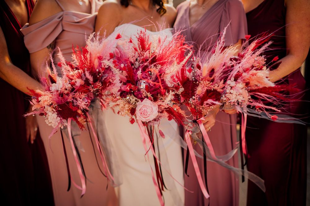 Pink and red floral wedding bouquets arranged in a row against a dark background.